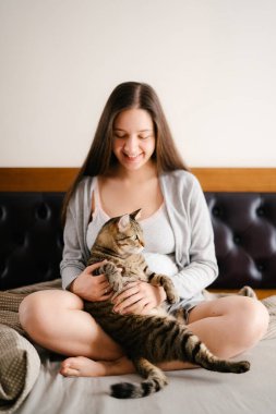 Hamile kadın kediyle yatakta oturuyor.