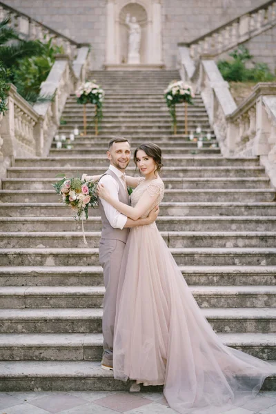 Η νύφη αγκαλιάζει τον γαμπρό στα πέτρινα σκαλιά κοντά στην παλιά βίλα — Φωτογραφία Αρχείου