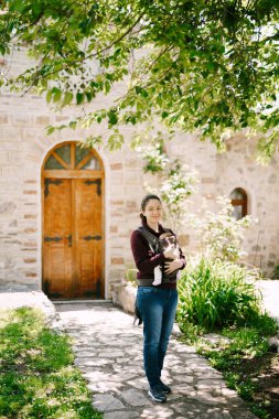 Annem taş bir evin avlusunda kaldırım taşlarının üzerinde duran askı içinde bir bebeğe sarılıyor.