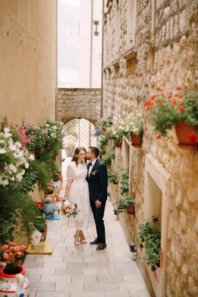A menyasszony és a vőlegény egy keskeny, virágcserepekkel díszített utcában sétálnak. — Stock Fotó
