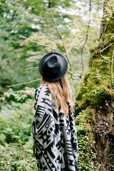 戴着帽子和披风的女人站在公园的一棵树旁，树上覆盖着苔藓。背景色 — 图库照片