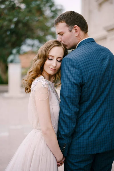 Sposo bacia la parte superiore della testa della sposa, mentre tenendo la mano. Ritratto — Foto Stock