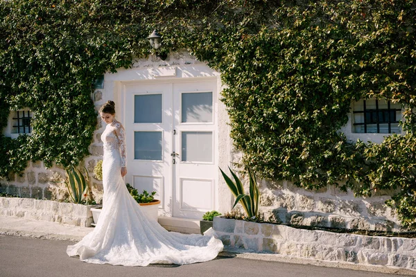 A menyasszony sellő ruhában áll egy borostyánnal borított épület ajtaja előtt. — Stock Fotó