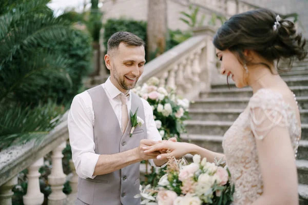 Le marié souriant met l'anneau sur le doigt de la mariée tout en se tenant debout sur les marches — Photo