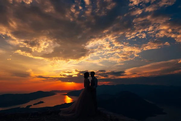 Groom and bride stand on the mountain against the background of sunset — Stock Photo, Image