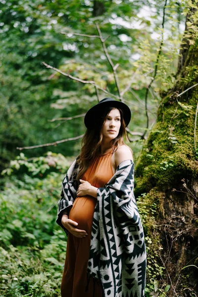 妊娠中の女性は腹を抱擁しながら公園の苔むした木の近くに立って — ストック写真