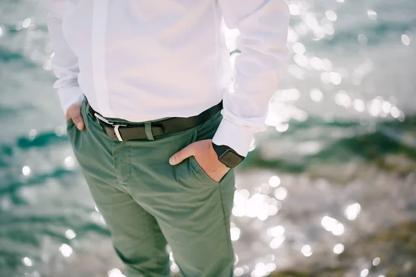 Man in green trousers stands over sparkling water with his hands in his pockets. Close-up