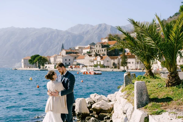 Pengantin wanita dan pengantin pria berpelukan sambil berdiri di atas batu-batu di lepas pantai Perast. Montenegro — Stok Foto