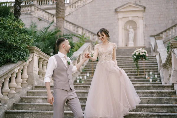 Groom ajuda a noiva a descer os degraus de pedra — Fotografia de Stock