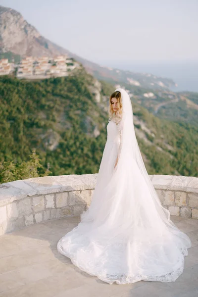Brud i en vit spets klänning står på ett observationsdäck mot en bakgrund av berg — Stockfoto