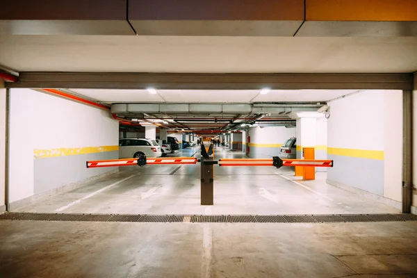 Ingang met een slagboom naar een grote ondergrondse parkeerplaats met geparkeerde auto 's — Stockfoto