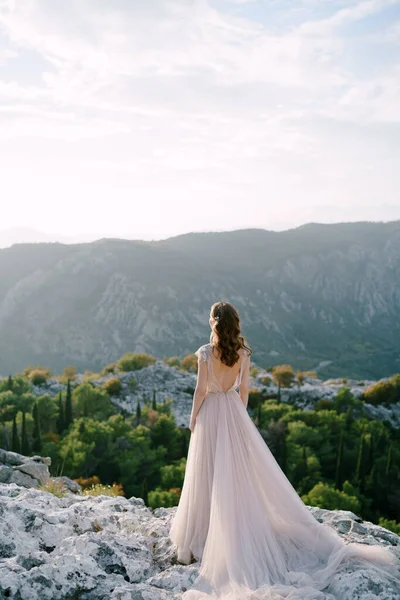 Bruid staat op een rotsachtige berg en kijkt uit over de baai — Stockfoto