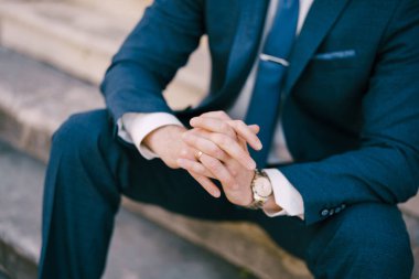 Mavi takım elbiseli damat taş basamaklarda oturuyor. Yakın plan.