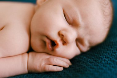 Bebek, elleri yanağının altında mavi bir battaniyede uyuyor. Kapat.