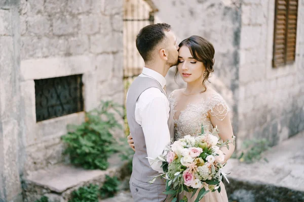 Bräutigam küsst Braut Stirn in der Nähe des Steingebäudes Porträt — Stockfoto