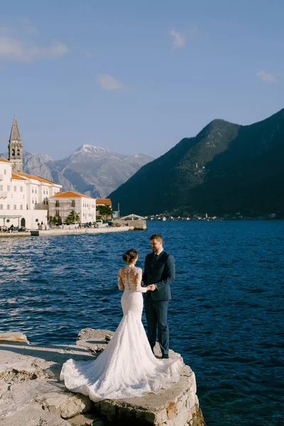Ženich a nevěsta stojí na kamenném molu na pozadí starobylého města Perast — Stock fotografie