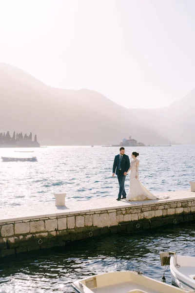 Panna młoda i pan młody spacerują molo na tle wysp w pobliżu Perast. Czarnogóra — Zdjęcie stockowe