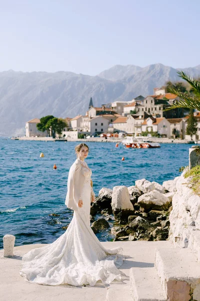 Panna młoda w długiej białej sukni syreny stoi na molo u wybrzeży Perast — Zdjęcie stockowe