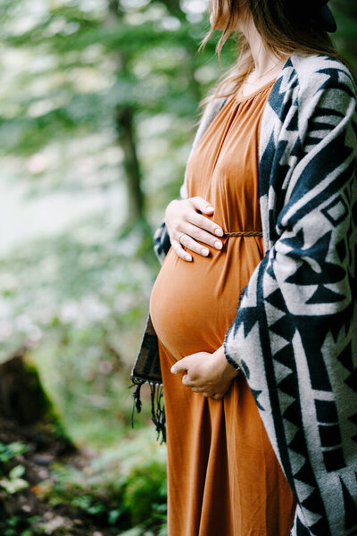 Pregnant woman hugs her belly with her hands in the park 