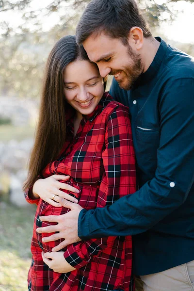 Un uomo sorridente abbraccia una donna incinta da dietro. Primo piano — Foto Stock