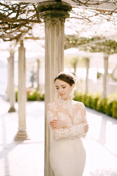 Νύφη με φόρεμα στέκεται κοντά σε μια στήλη σε ένα παλιό αίθριο. Πορτρέτο — Φωτογραφία Αρχείου