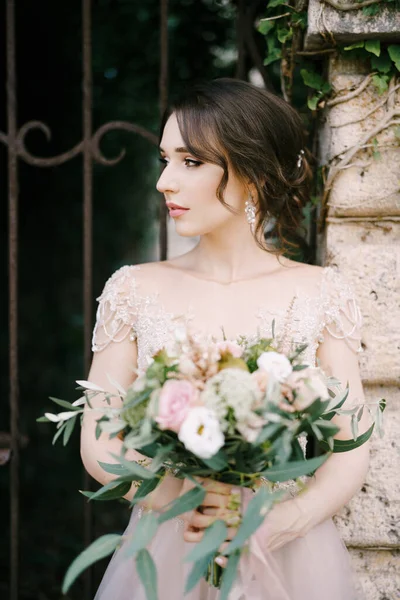 Noiva com buquê de flores fica no portão forjado. Retrato — Fotografia de Stock