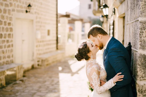 Ženich políbí nevěstu v blízkosti šedé kamenné zdi starého domu — Stock fotografie