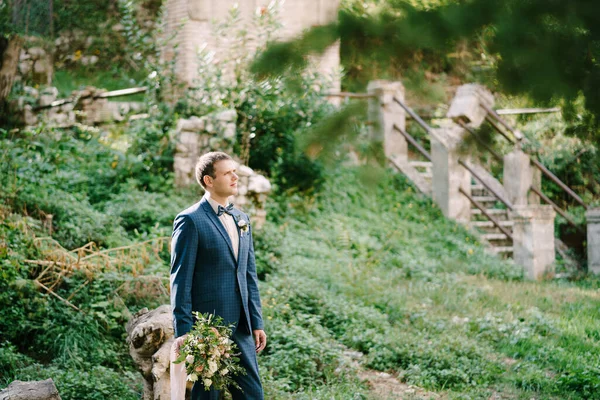 Bräutigam mit Blumenstrauß steht neben dem alten Gebäude im Garten. Nahaufnahme — Stockfoto