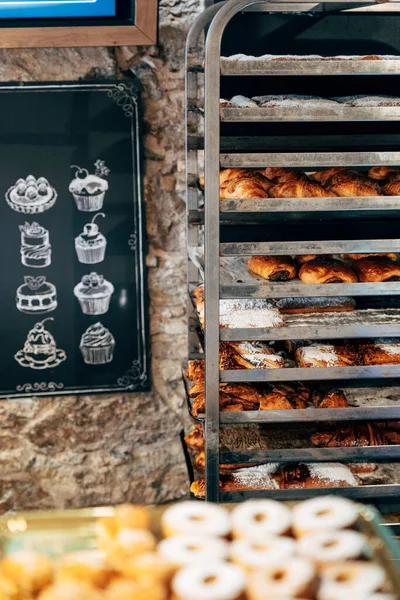 Roti manis ditaburi dengan bubuk gula terletak di rak-rak di toko kue — Stok Foto
