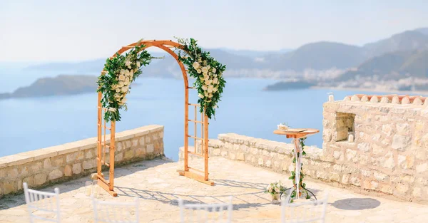 Arco de casamento de madeira decorado com flores fica no deck de observação acima do mar — Fotografia de Stock