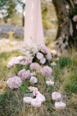 Cam kavanozlarda yanan mumlar, çiçeklerle süslenmiş, korulukta bir ağacın yanında duran