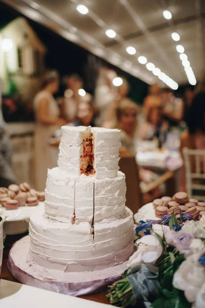Krájený svatební dort vedle makarónových dortů stojí na stole — Stock fotografie