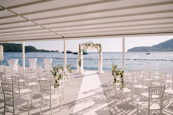 해변에 있는 하얀 캐노피 밑에서 결혼식 아치 앞에 하얀 의자들이 줄지어 서 있다 — 스톡 사진