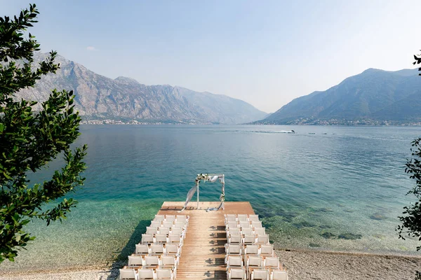 Düğün kemerinin önündeki rıhtımdaki sıra sıra sandalyeler denizin ve dağların arka planına karşı.