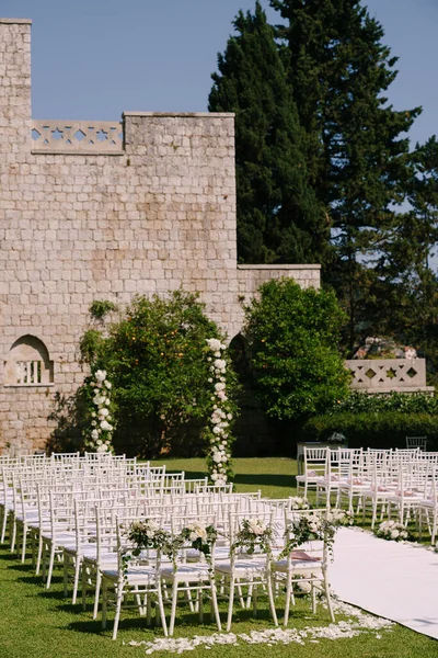 Semi-arco de la boda se encuentra cerca de una pared de ladrillo en el jardín frente a filas de sillas — Foto de Stock