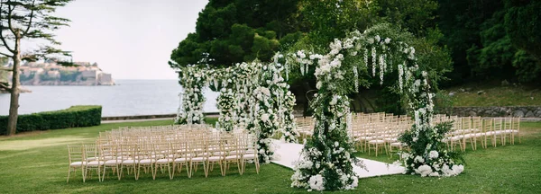 Fila de arcos de boda se encuentra en un césped verde rodeado de sillas cerca del agua — Foto de Stock