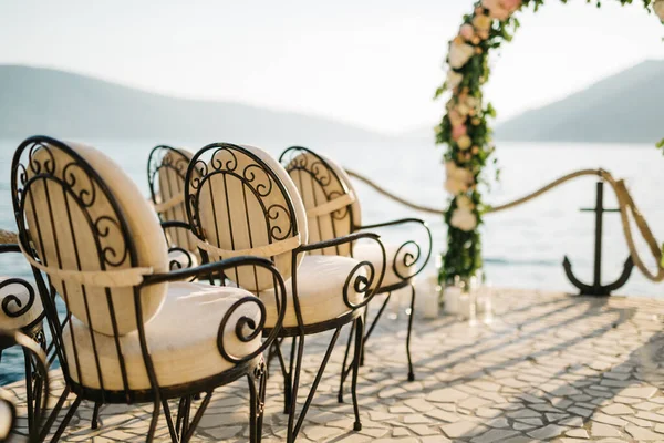 Row of padded chairs in front of a wedding arch on a cobbled pier — Stock Photo, Image