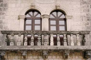 Balkonu oyulmuş taş balkon ve pilasterli kahverengi cam kapılar.