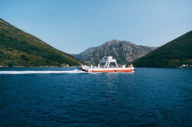 Mavi denizde, dağların arka planına karşı küçük bir tekne yelken açar.