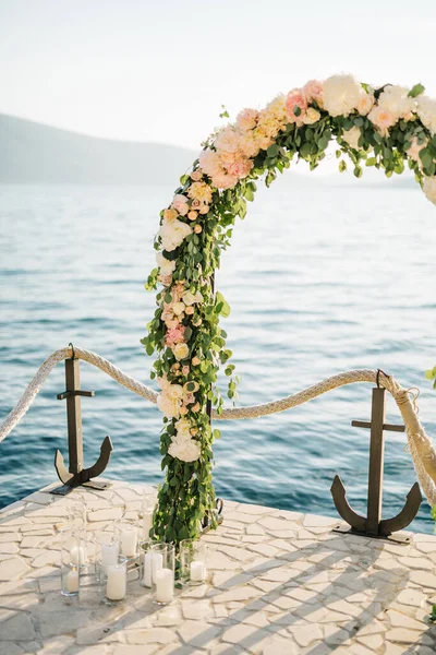 Bröllopsbåge står på en stenlagd brygga vid ett rep staket med ankare — Stockfoto