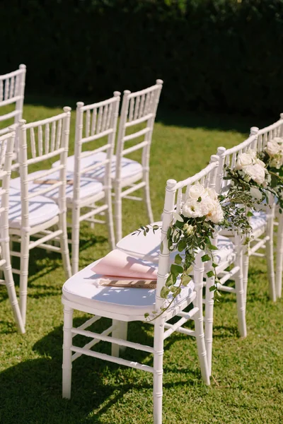 Row of white chairs decorated with bouquets of flowers stands on a green lawn — Stock Photo, Image