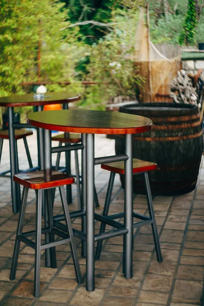 High metal table with wooden top and low stools in a street cafe — Foto Stock