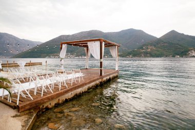 Bir sıra sandalyenin önündeki iskelede düğün tentesi. Yan görünüm