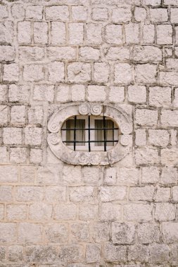 Binanın eski taş cephesinde kafesi olan küçük oval pencere.