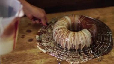 Pasta şefi kremalı çikolatalı kekin üzerine mermer ayna kreması dağıtıyor.