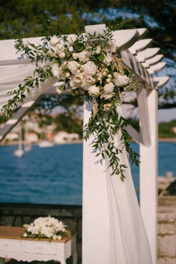Düğün örtüsünün köşesinde, beyaz çiçeklerle süslenmiş, denizin arka planında.