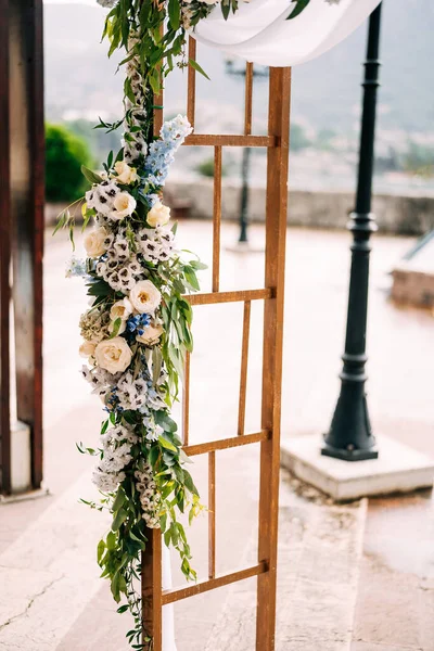 Çiçekler, beyaz bez ve yeşil dallarla süslenmiş dikdörtgen ahşap bir kemer parçası.