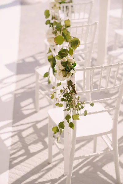 Respaldos de las sillas blancas están decoradas con flores blancas y ramas verdes — Foto de Stock