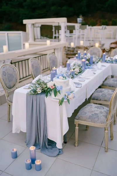 Gâteau de mariage blanc superposé décoré de fleurs se tient sur une table avec des bougies allumées — Photo