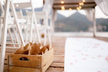 Üzerinde çiçek yaprakları olan yuvarlanmış kağıt torbalarla ahşap kutu iskemlelerin yanında duruyor.